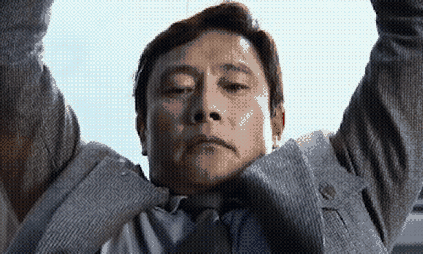 Close-up shot of a guy in a suit lifting something heavy over his head.