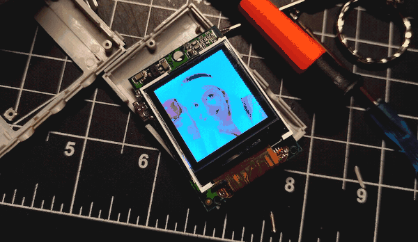 The photo keychain partially disassembled on my desk. The screen, still on, displays a stock image of a smiling woman in a sweatband holding an apple up to her temple.